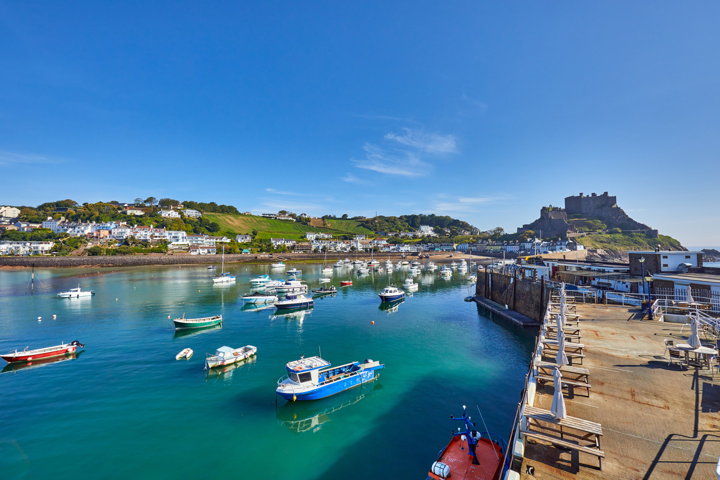 Gorey Harbour with fishing and pleasure boats, the pier bullworks and Gorey Castle in the background with blue sky. Jersey, Channel Islands, UK