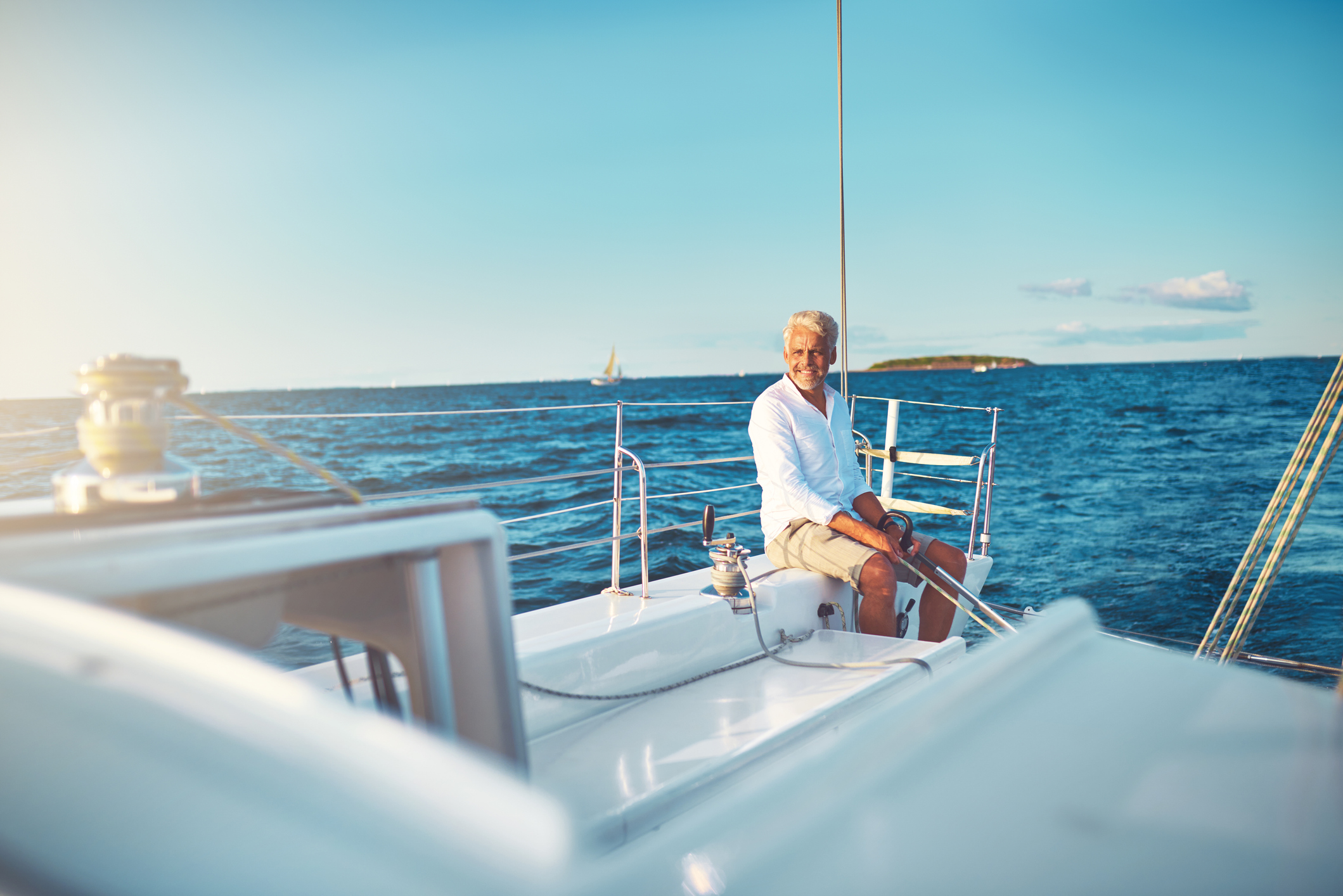 Smiling mature man sitting alone on the deck of his boat while sailing on the open ocean on a sunny day