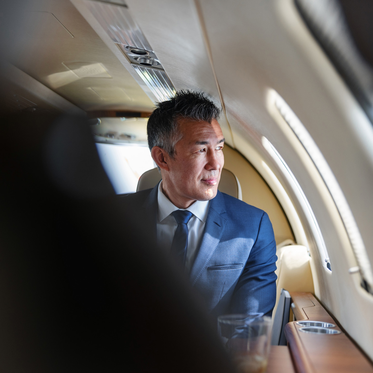 Sophisticated businessman looking out the window, reflecting in a luxurious private jet atmosphere.