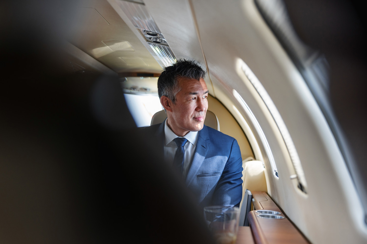 Sophisticated businessman looking out the window, reflecting in a luxurious private jet atmosphere.