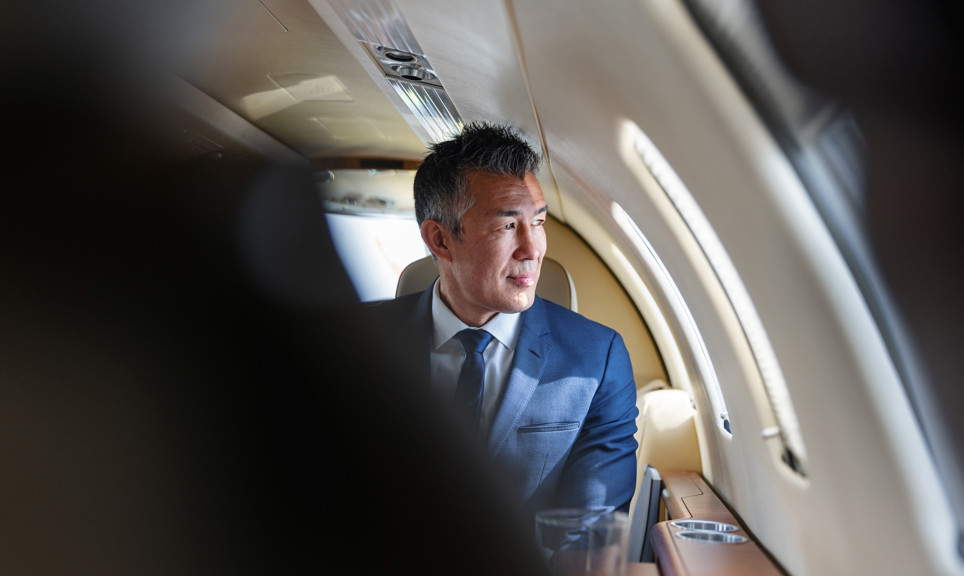 Sophisticated businessman looking out the window, reflecting in a luxurious private jet atmosphere.
