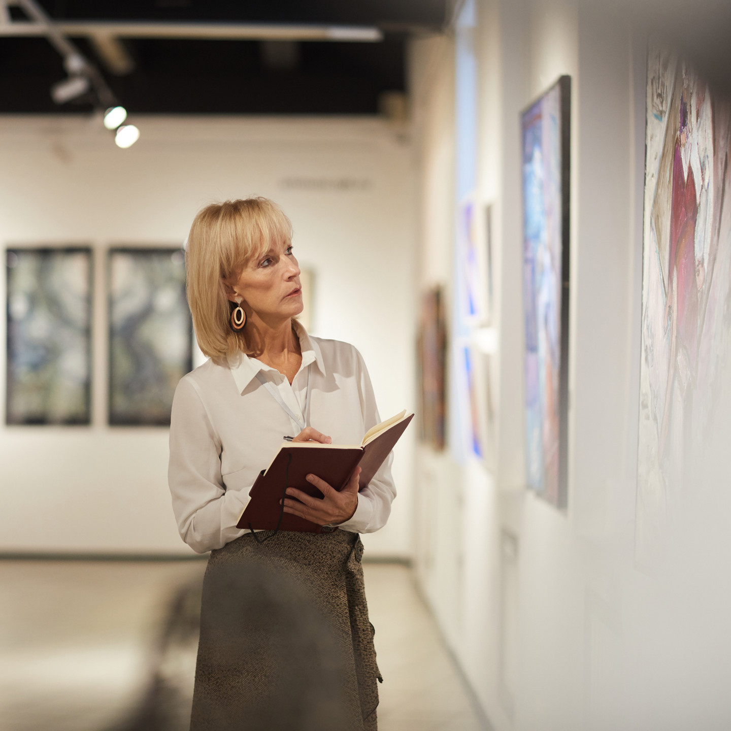 Waist up portrait of elegant mature woman looking at paintings in art gallery hall and enjoying museum exhibition, copy space
