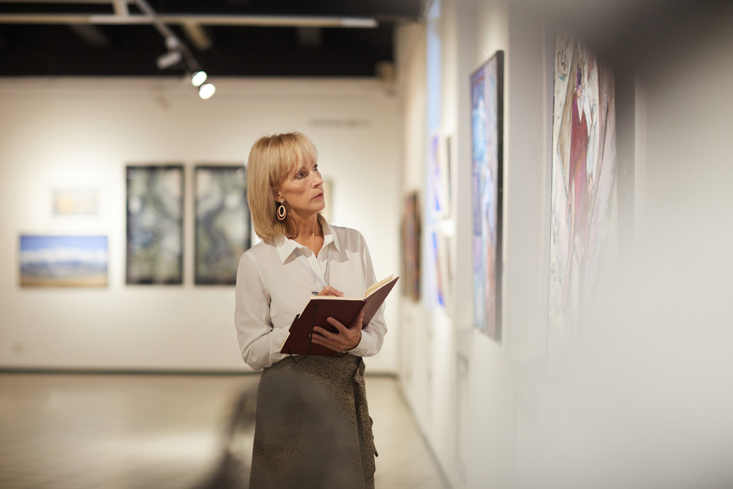 Waist up portrait of elegant mature woman looking at paintings in art gallery hall and enjoying museum exhibition, copy space